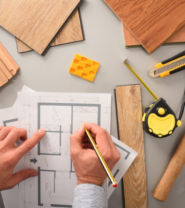 Hands on designer on desk writing on blueprints developing interior project with wood samples and tools. Top view.