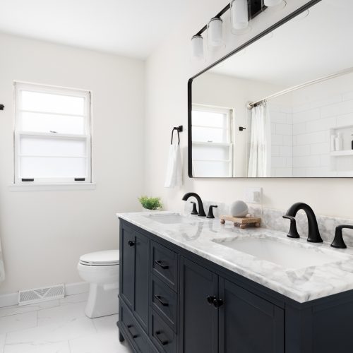 A beautiful bathroom with a dark blue vanity cabinet, marble countertop, and large mirror below a light.